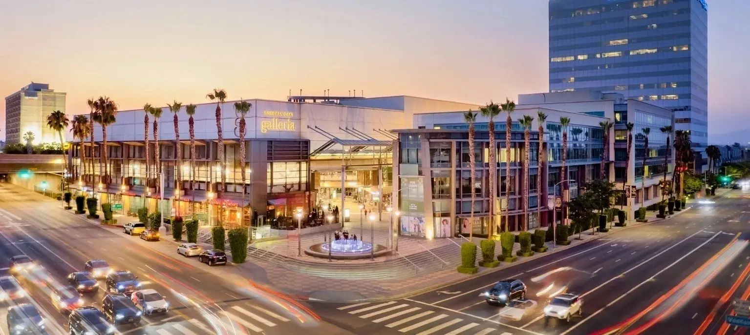 Shopping center at busy urban intersection, dusk.